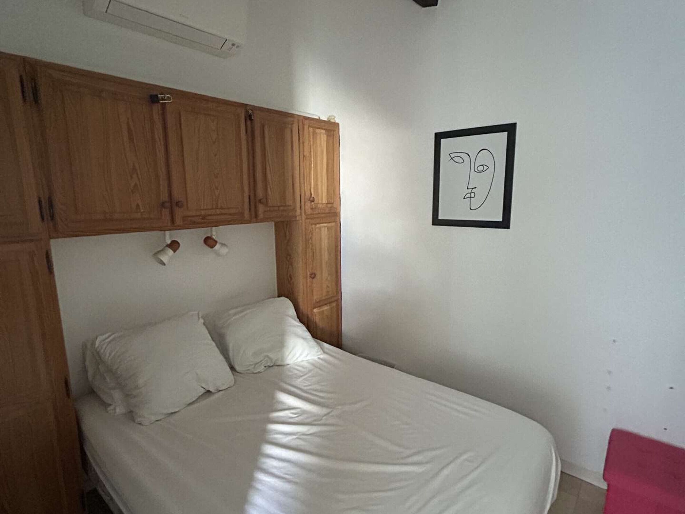 A single bed with a wooden headboard, a white wall, and a framed picture.