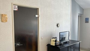Ein Zimmer mit geschlossener Tür, einem kleinen Schrank mit einem Computer und einer Wanduhr.