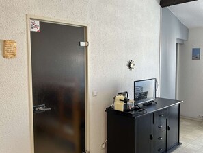 Ein Zimmer mit geschlossener Tür, einem kleinen Schrank mit einem Computer und einer Wanduhr.