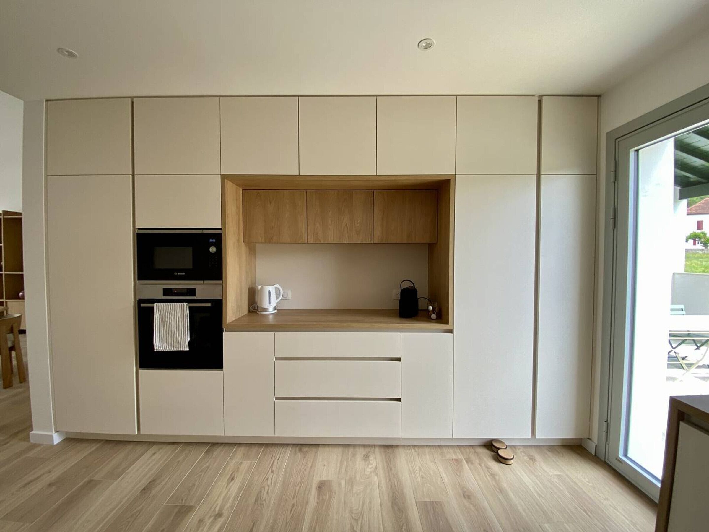A modern kitchen with built-in appliances, a wooden countertop, and a large window.