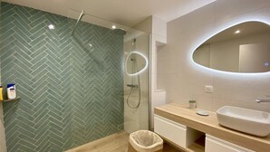 Een moderne badkamer met een backsplash van visgraatmozaïek, een douche met glazen wanden, een houten wastafelmeubel en een grote spiegel.