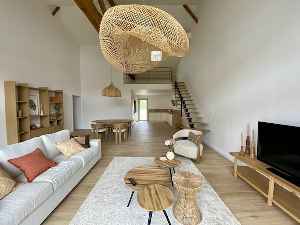 A spacious living room with a sofa, coffee table, TV stand, and a staircase leading to an upper level. - Terraced house in city center - 4 guests (Louhossoa)