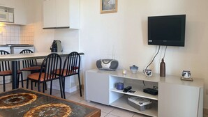 Un ambiente compatto con angolo ristoro, cucina e televisore a parete.