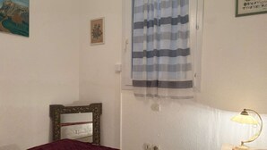 Camera da letto con un letto, una lampada da comodino, una finestra con tende, un quadro incorniciato e un interruttore della luce a parete.