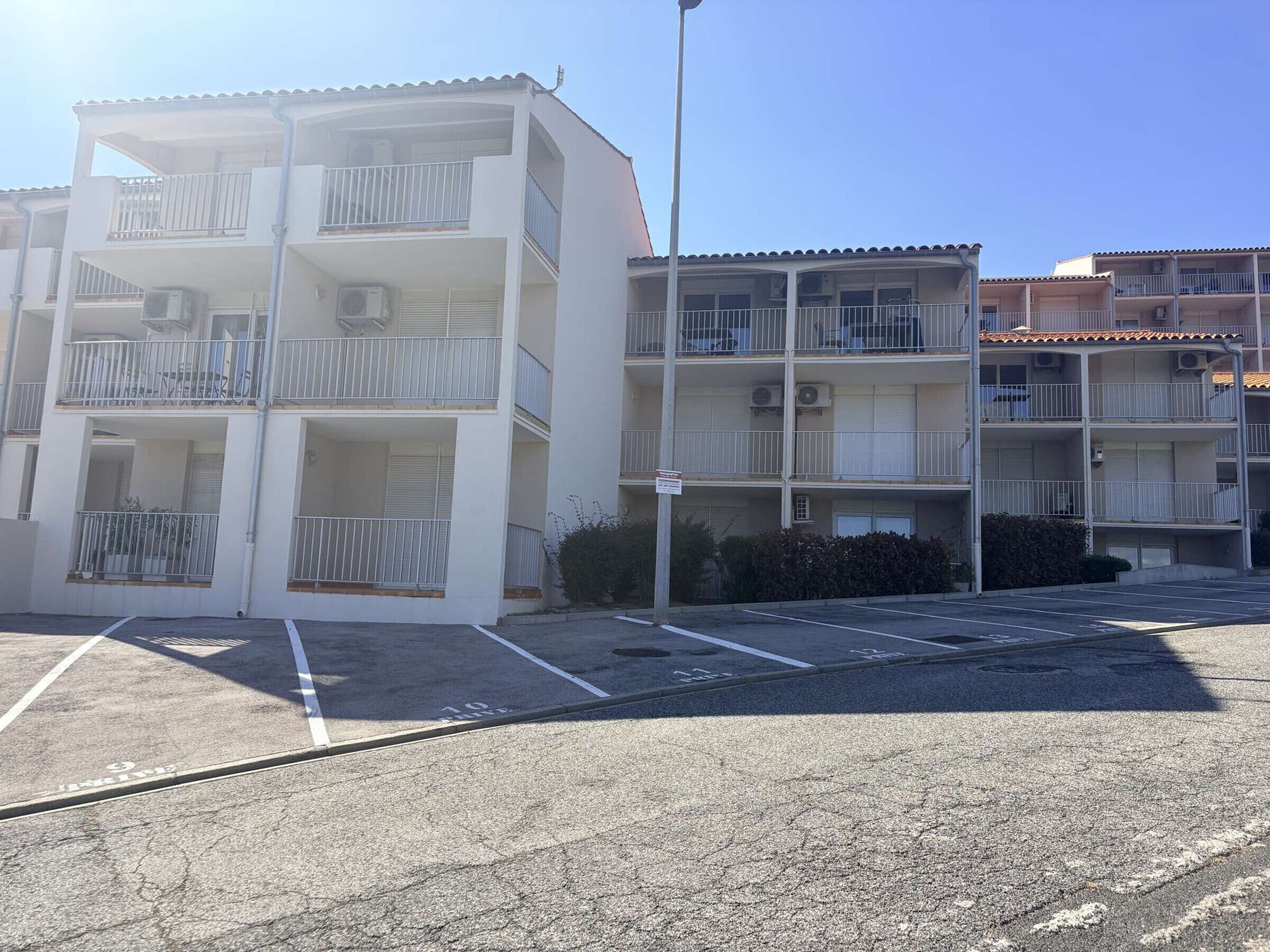 A multi-story residential building with balconies, air conditioning units, and a parking lot.
