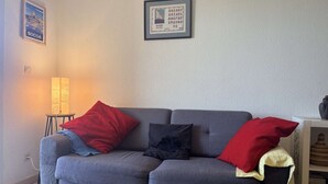 Un divano grigio con cuscini rossi e neri, un tavolino con una lampada e un quadro appeso al muro.