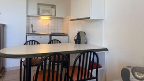Una cucina compatta con mobili bianchi, un forno a microonde, un piano cottura e una macchina da caffè. C'è un tavolo da pranzo con quattro sedie.