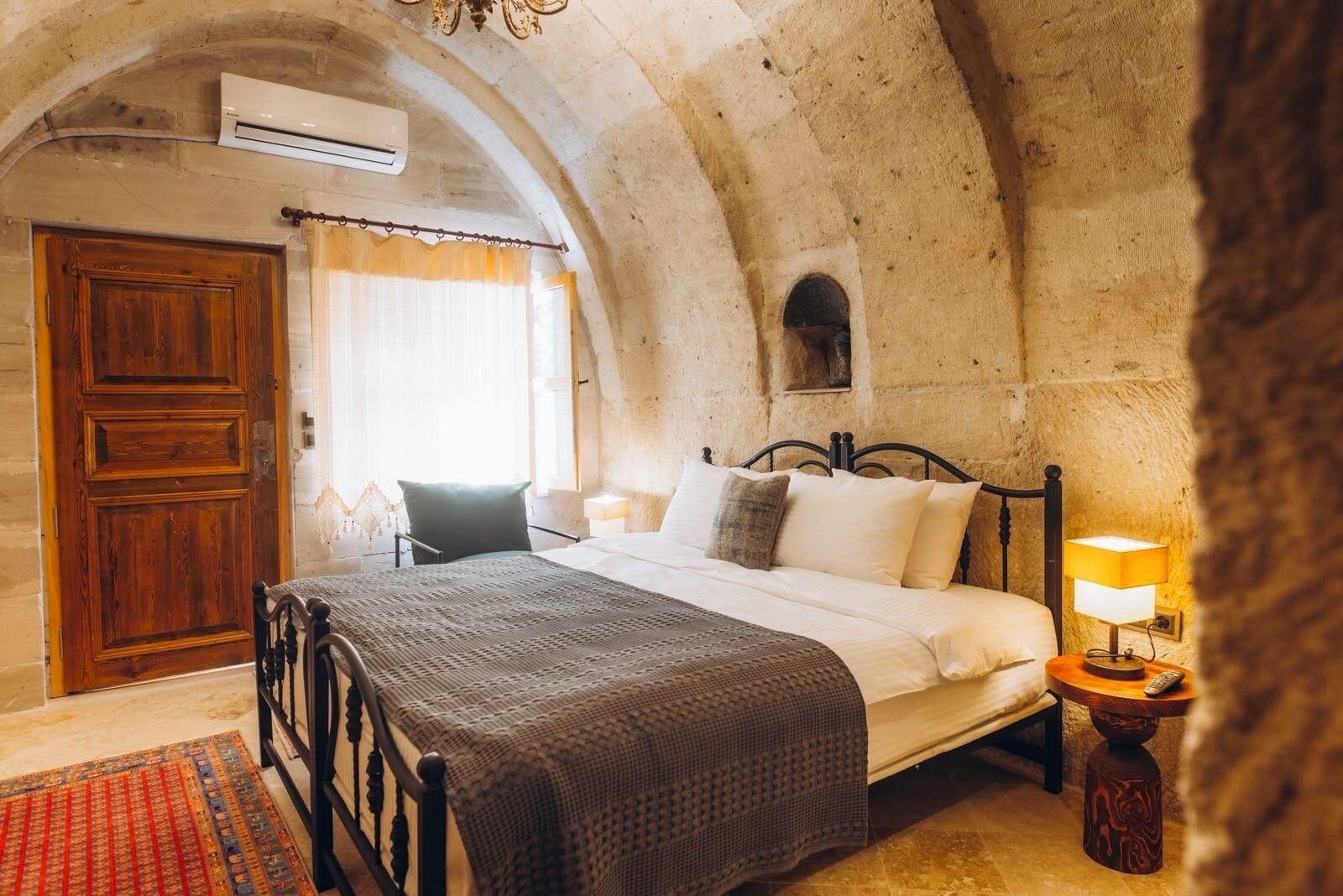 Un dormitorio con cama, una silla, una mesita de noche y un techo de piedra en arco.