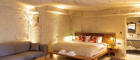 Un dormitorio con cama, sofá, mesita de noche y baño visible a través de un arco.
