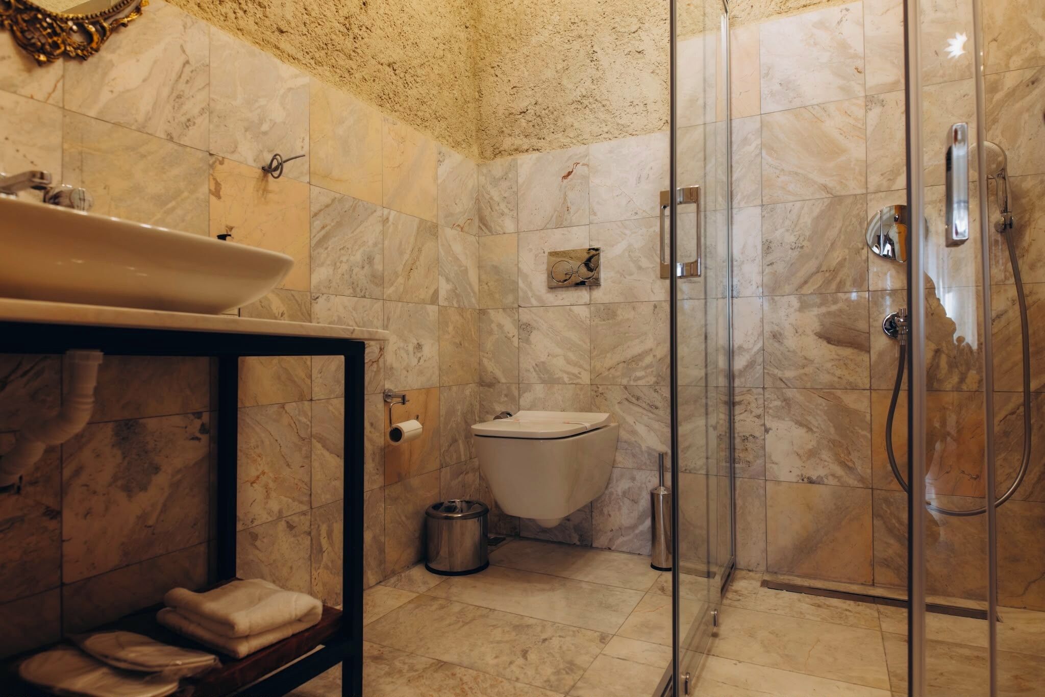 Un baño con piso de mármol, ducha con cerramiento de vidrio, inodoro y lavamanos con encimera de mármol.