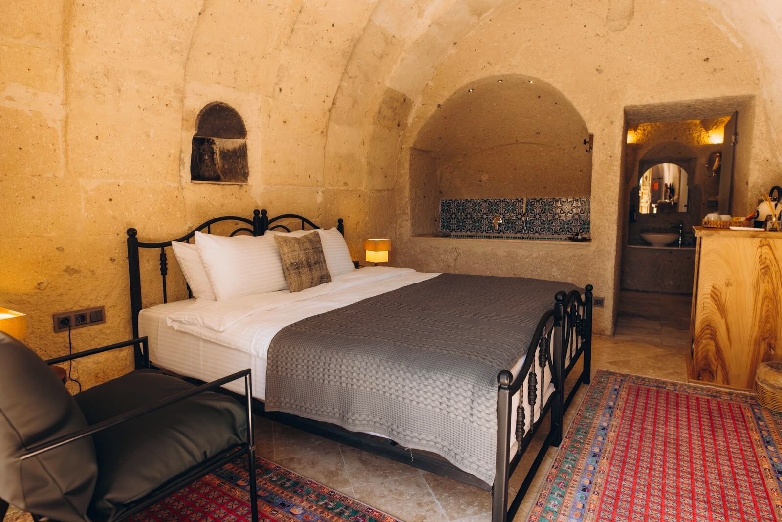A bedroom with a bed, a chair, a patterned rug, and a tiled backsplash.