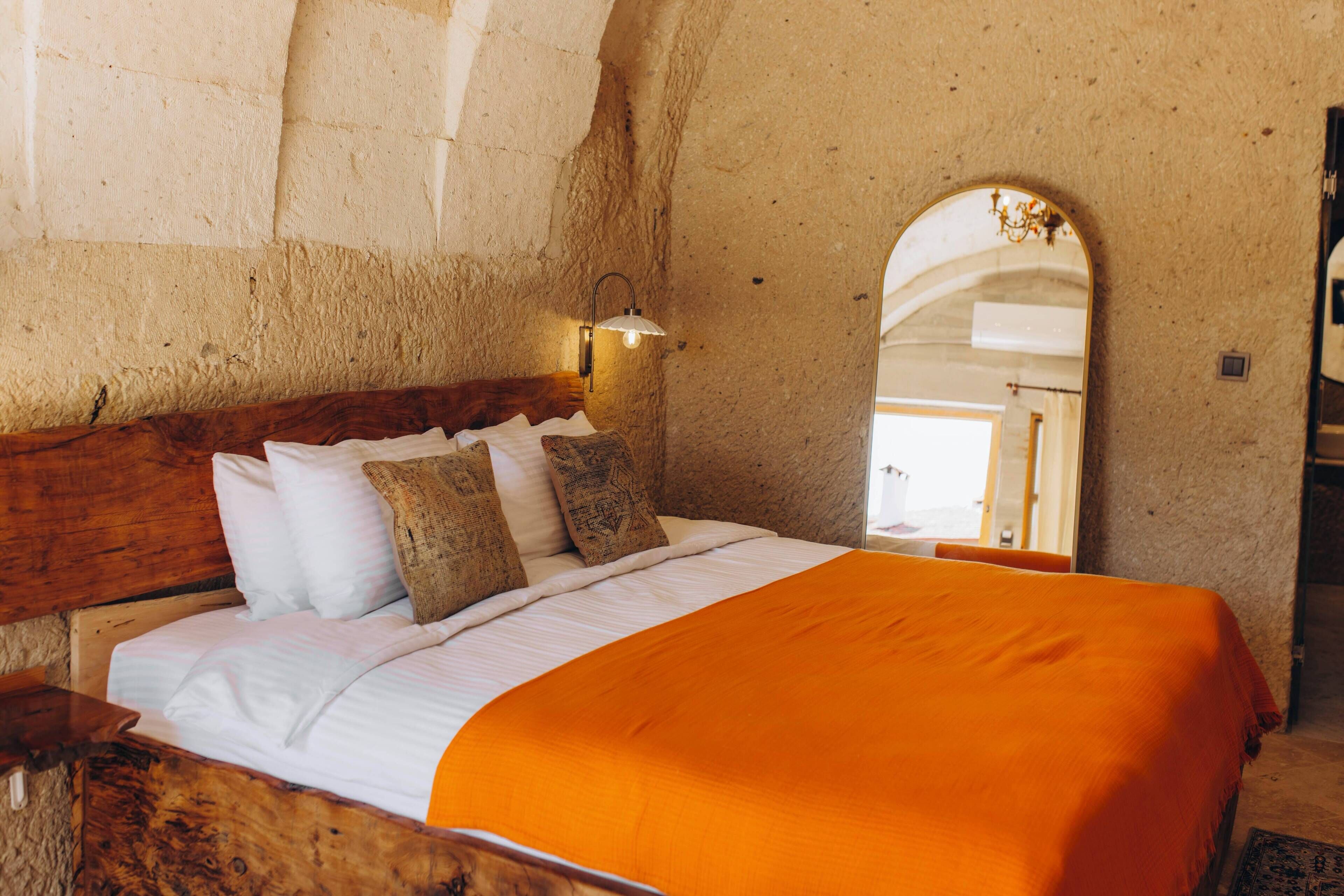 A bedroom with a wooden headboard, a bed with white and orange bedding, and a stone wall.