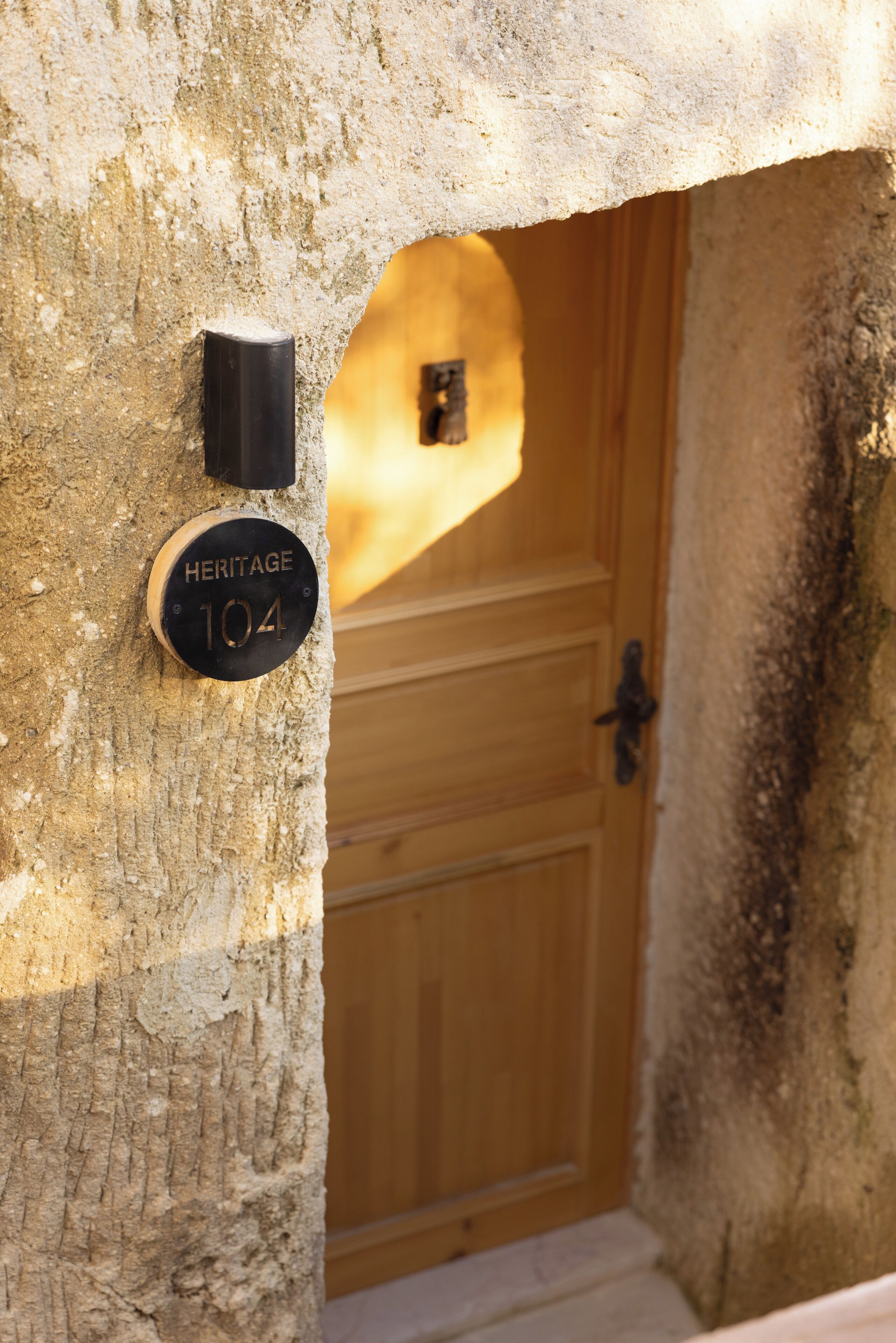 A wooden door with a black handle, a doorbell, and a sign reading 'Heritage 104' on a textured wall.