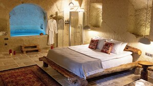 A bedroom with a large bed, a wooden headboard, a built-in bathtub, and a walk-in shower. - Soul of Cappadocia Hotel (Urgup)