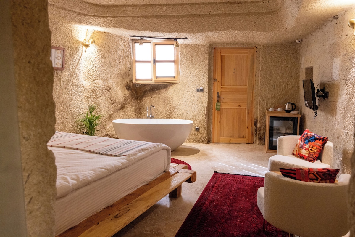 Una habitación rústica con una bañera grande, una cama de madera, una silla pequeña y una alfombra roja.