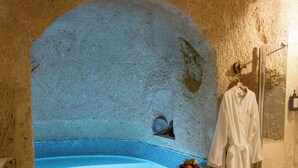 A stone-walled bathroom with a bathtub, a wooden bench, candles, and a robe hanging on the wall. - Soul of Cappadocia Hotel (Urgup)