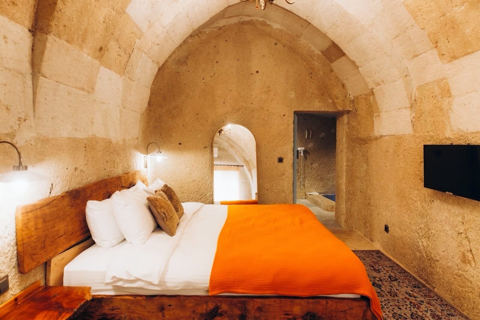 Una habitación con pared de piedra, una cama de madera, un televisor de pantalla plana y una mesita.