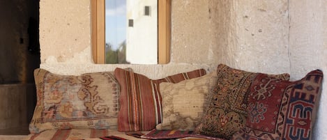 A rustic wooden bench with patterned cushions, a small window, and a stone wall with a number plaque.