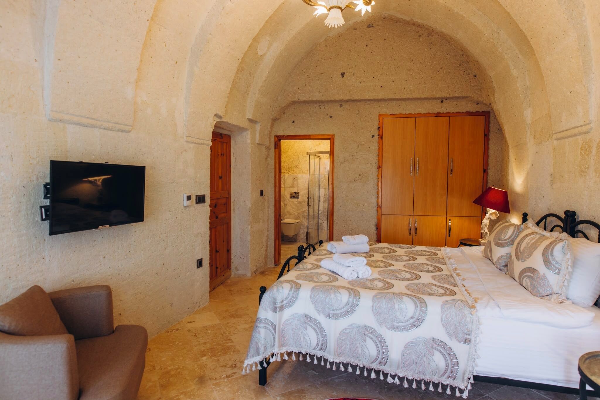 A bedroom with a bed, a TV, a sofa, and a wooden wardrobe.