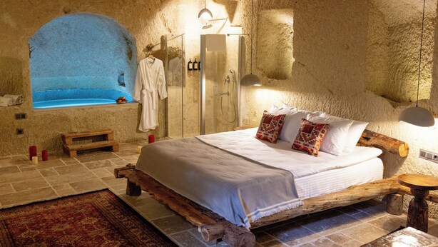 A bedroom with a large bed, a wooden headboard, a built-in bathtub, and a stone wall. - Soul of Cappadocia Hotel (Urgup)