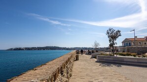 A coastal walkway with a stone wall, a tree, and a building with a red roof. - (018) Le Nid des Remparts (Antibes)
