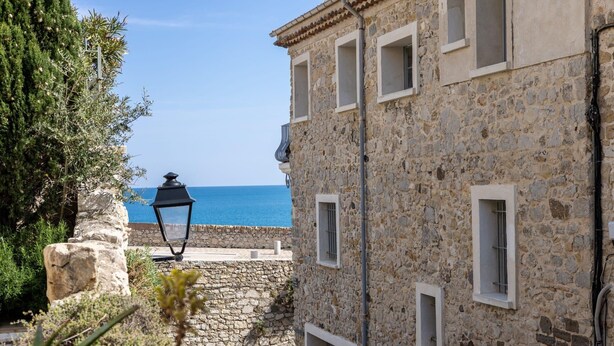 A stone building with a view of the sea, a stone wall, and a lamp post. - (018) Le Nid des Remparts (Antibes)