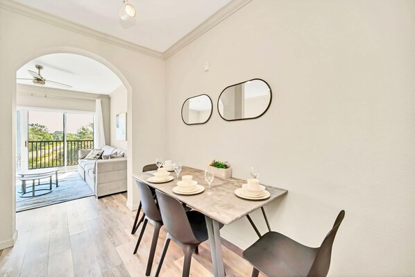 Un coin repas avec une table dressée pour quatre personnes, un canapé et, au fond, une vue sur une terrasse extérieure accessible par une arche.
