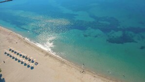 An aerial view of a beach with clear turquoise water, a sandy shore, and rows of beach umbrellas. - Hotel Elena -sunny Seaside Balcony Suite in Skyros (Skiros)