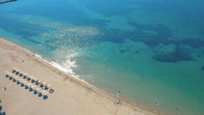 An aerial view of a beach with clear turquoise water, a sandy shore, and rows of beach umbrellas. - Hotel Elena - Cozy Seaside Double Suite in Skyros (Skiros)