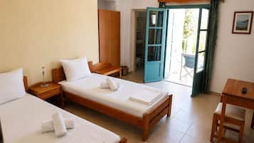 Habitación de hotel con dos camas individuales, un armario de madera, una mesita pequeña, una silla y un baño visible a través de una puerta abierta.
