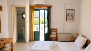 Hotellihuone, jossa on kaksi sänkyä, työpöytä, tuoli, pieni pöytä, ikkuna, jossa on verhot, ja kylpyhuone, joka näkyy avoimesta ovesta.