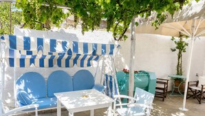 Un espace patio aménagé avec un canapé bleu, des chaises blanches, une petite table et un tonneau vert.