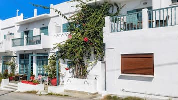 A white building with a balcony, a wooden door, and a small table with chairs outside.