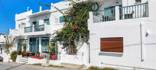 A white building with a balcony, a wooden door, and a small table with chairs outside.