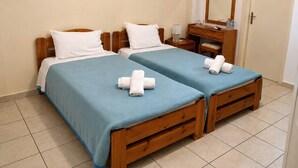 Ein Doppelzimmer mit zwei Betten, jeweils mit blauer Bettdecke und weißen Kissen, einem hölzernen Schminktisch, einem Spiegel und einer Tür.