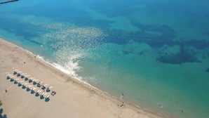 Ein Luftbild eines Strandes mit klarem türkisblauem Wasser, einem Sandstrand und Reihen von Strandsonnenschirmen.