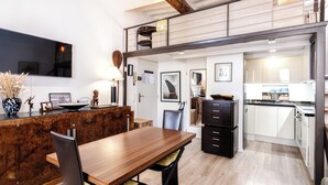 Una cucina moderna con un piano di lavoro in legno, un'area pranzo con tavolo e sedie in legno, e un soppalco accessibile tramite una scala.