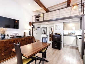 Eine moderne Küche mit Holzarbeitsplatte, ein Essbereich mit Holztisch und -stühlen sowie ein erhöhter Bereich mit einer Wendeltreppe.