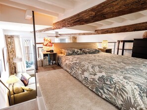 Ein Schlafzimmer mit einem großen Bett, Holzbalken, einem Schreibtisch mit Lampe und Blick ins Freie.