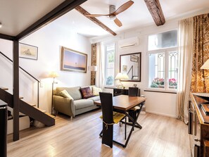 Ein modernes Wohnzimmer mit einer Couch, einem Esstisch, Stühlen, einer Treppe und einem Deckenventilator.