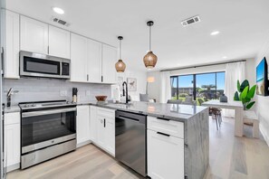 A modern kitchen with white cabinets, stainless steel appliances, and a large island. - Shuck It by Stay on 30a (Seacrest)