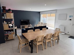 A modern living room with a wooden dining table, wicker chairs, a dark blue sofa, and a TV. - "Arago" Large family home close to the beach (Sète)
