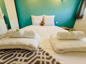 A neatly made bed with white pillows and a teddy bear, a pair of towels on the bed, and a patterned rug. - "Arago" Large family home close to the beach (Sète)