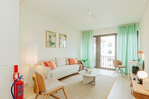 Ein modernes Wohnzimmer mit einer Couch, einem Couchtisch und Sesseln, einem Feuerlöscher und Blick durch eine Glastür.