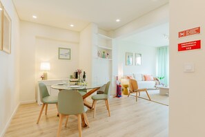 Ein modernes Wohnzimmer mit Essbereich, einer Couch und einem Couchtisch. Ein Feuerlöscher und ein Schild mit der Kennzeichnung des Notausgangs sind vorhanden.