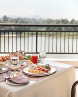 Mesa dispuesta para una comida, con diversos platos, vasos y una vista al lago y las montañas al fondo.