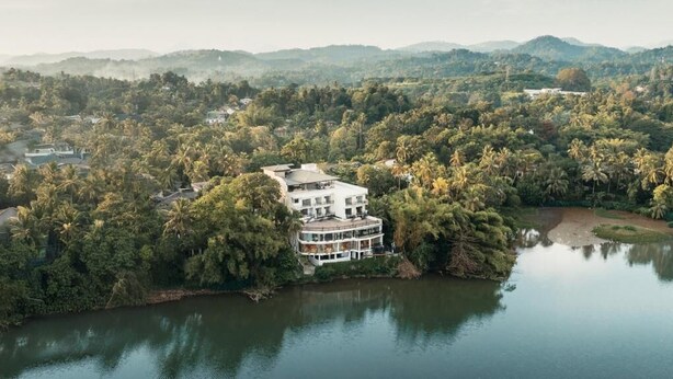 A multi-story building surrounded by dense greenery and a lake. - Royal Avenue Kandy (Kandy)