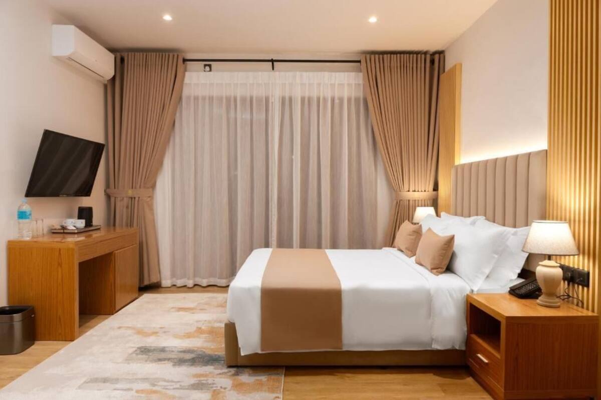 A hotel room with a bed, bedside table, lamp, TV, and curtains.