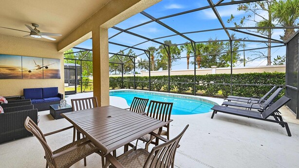 A covered outdoor area with a pool, lounge chairs, a table with chairs, and a sofa. - Upstay Disney Getaway With Pool Game Room (Davenport)