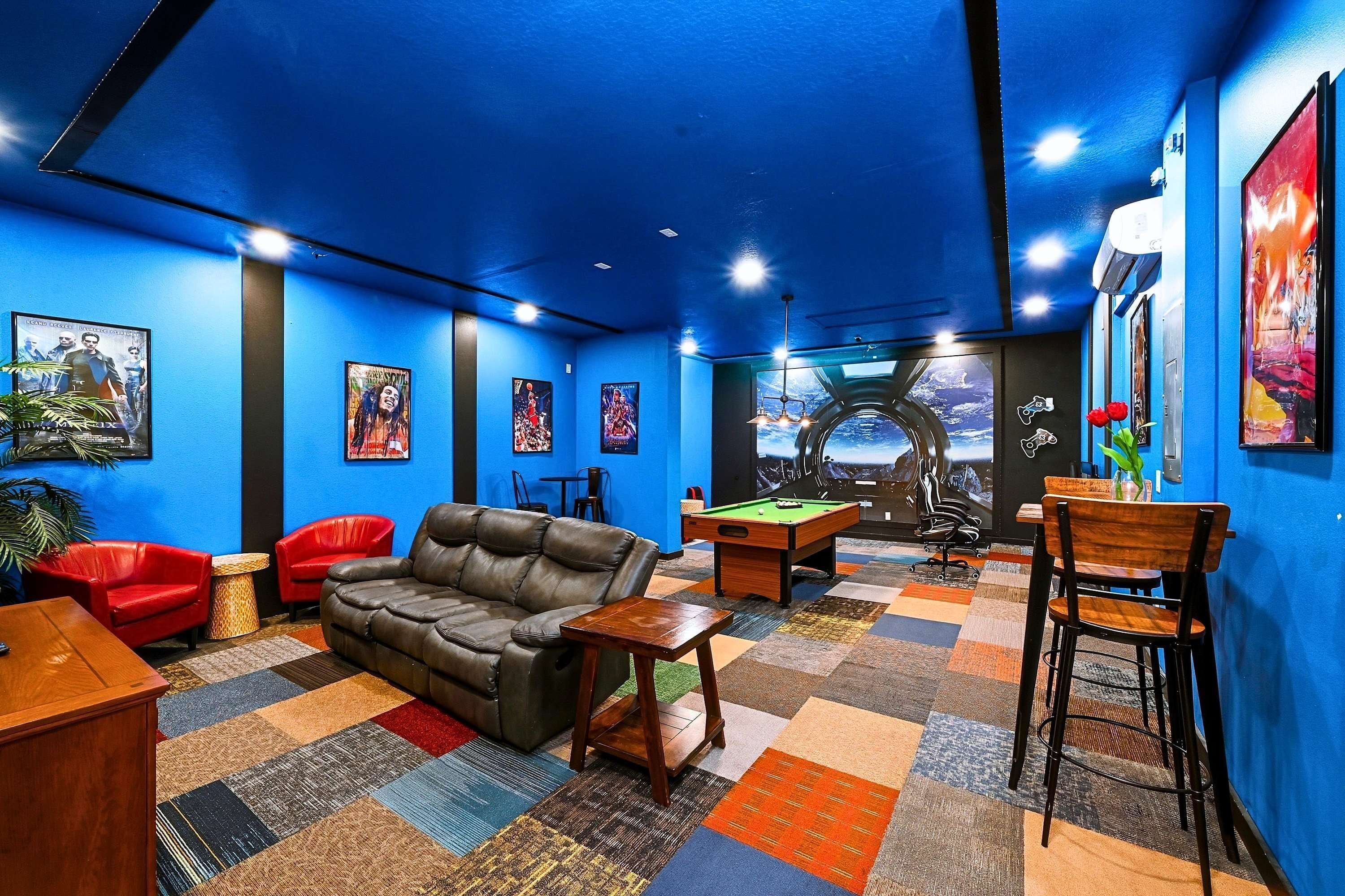 A room with a blue wall, a pool table, a leather couch, red chairs, and a wooden coffee table.